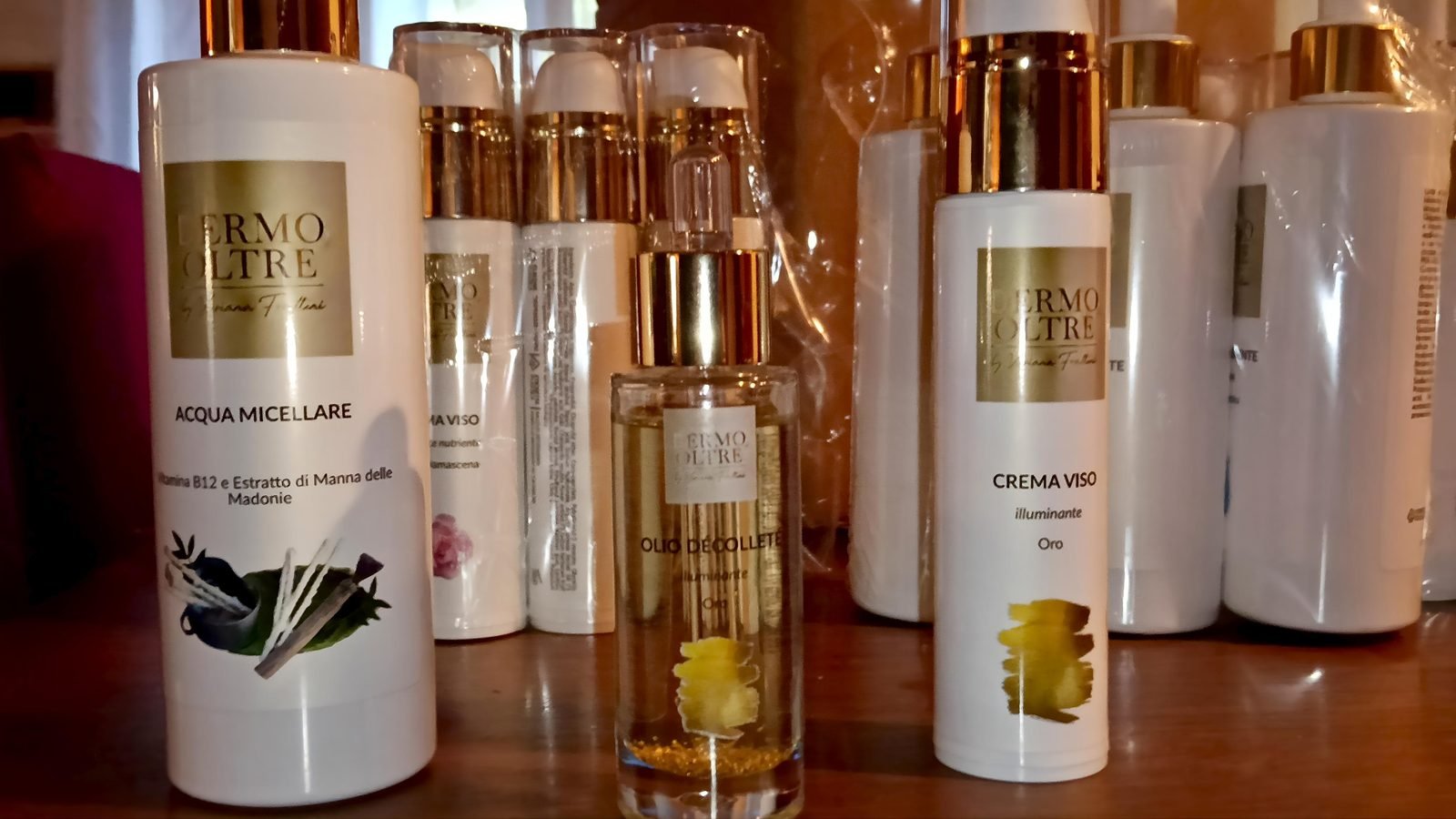 I flaconi Dermoltre allineati: acqua micellare, crema viso, olio décolleté. Bianchi con etichetta oro.